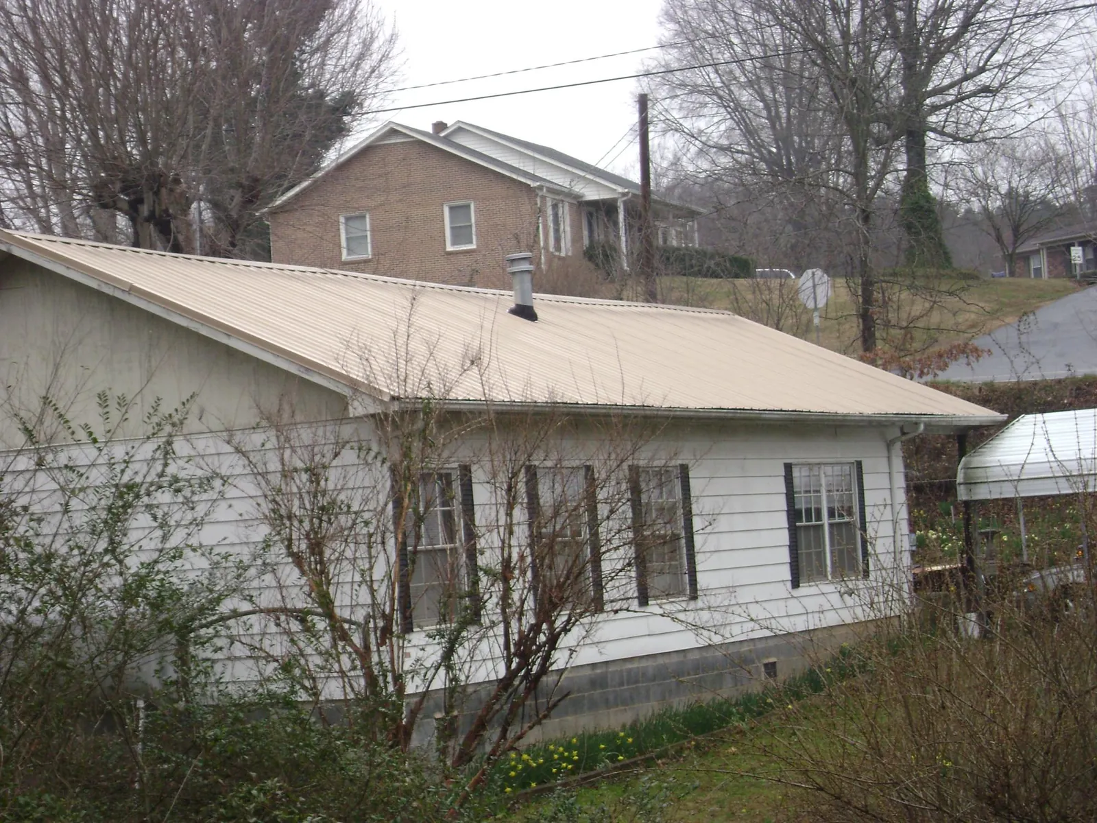 Tan metal roof on a white sided house set into a hillside — Commercial Roofing by Roofing Brothers in Andover
