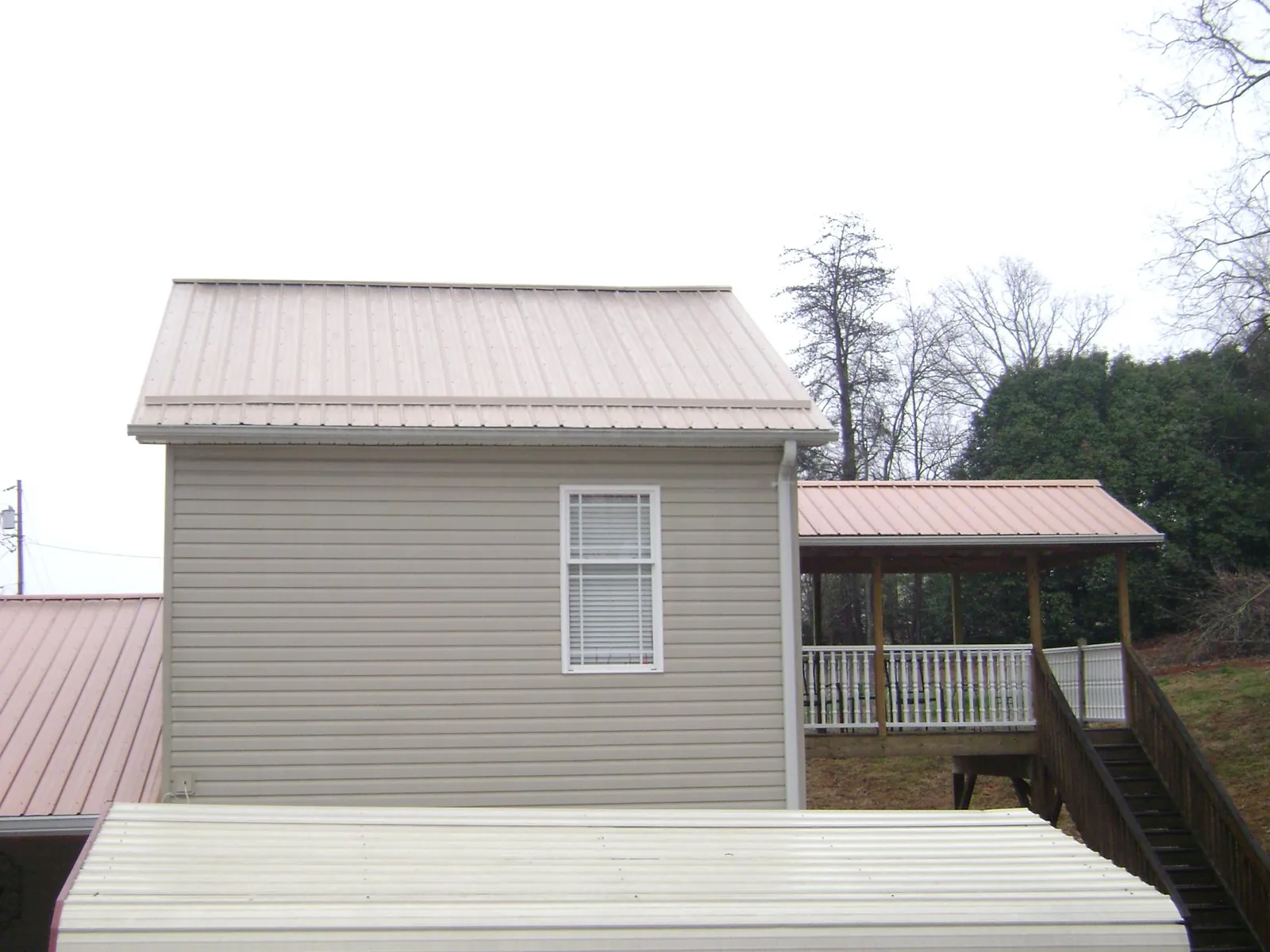Tan metal roofs on a two story addition and attached porch, from a Roof Replacement job in Andover